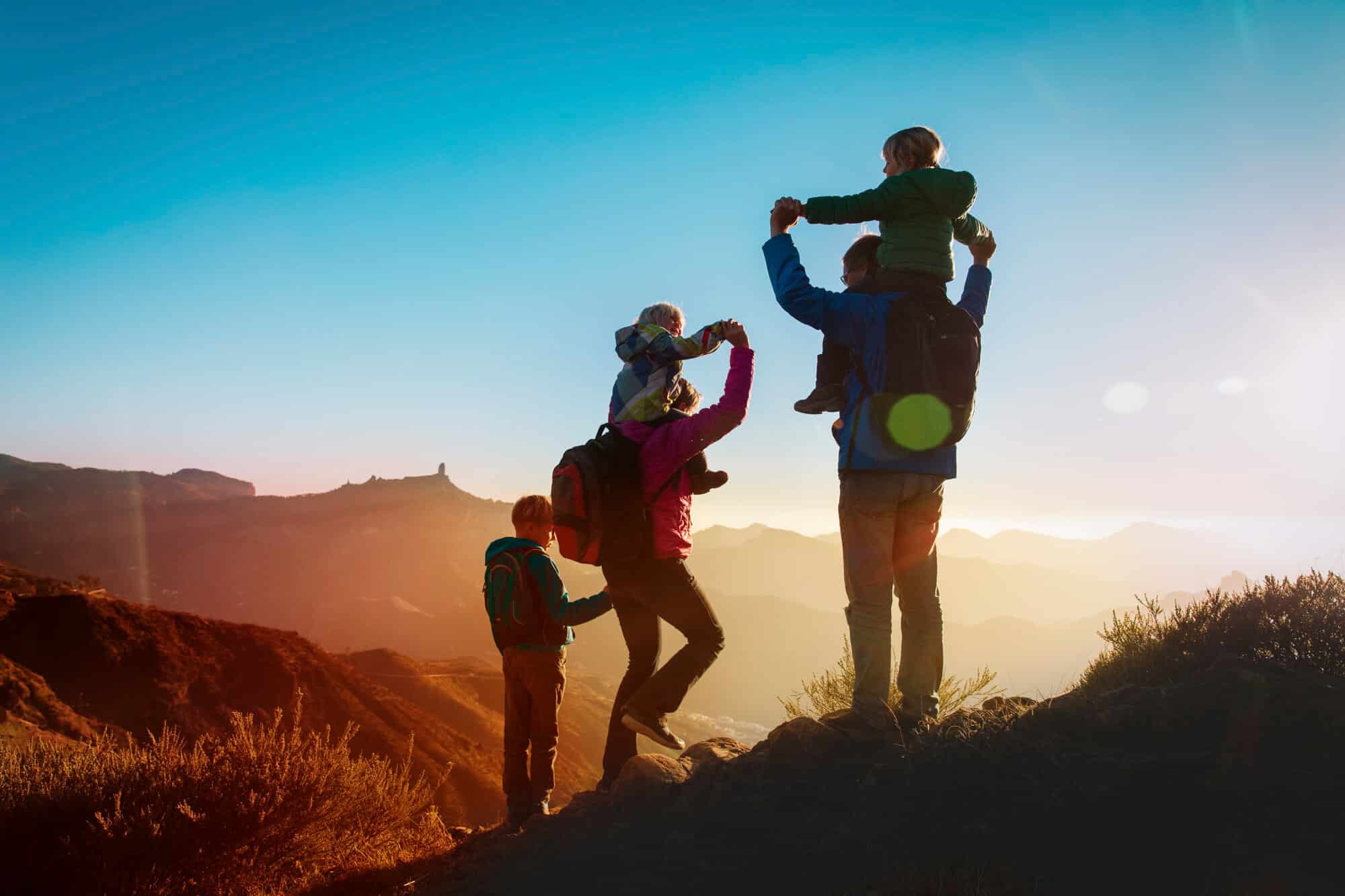 A family of hikers stands on a mountain ridge at sunset, holding hands and enjoying the view in Boise, ID