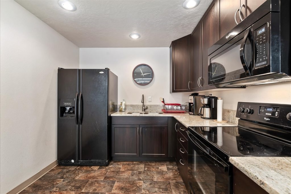 A modern kitchen with dark cabinets, black appliances, granite countertops, and a wall clock above the sink in Boise, ID